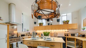 A modern kitchen with a central island, stainless steel appliances, wooden cabinets, and a unique hanging pot rack. - 5 bedroom accommodation in Rossendale (Rossendale)