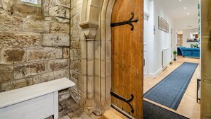 A stone wall with a wooden door, a bench, and a view into a modern living area with a blue sofa and a herringbone floor. - 5 bedroom accommodation in Rossendale (Rossendale)