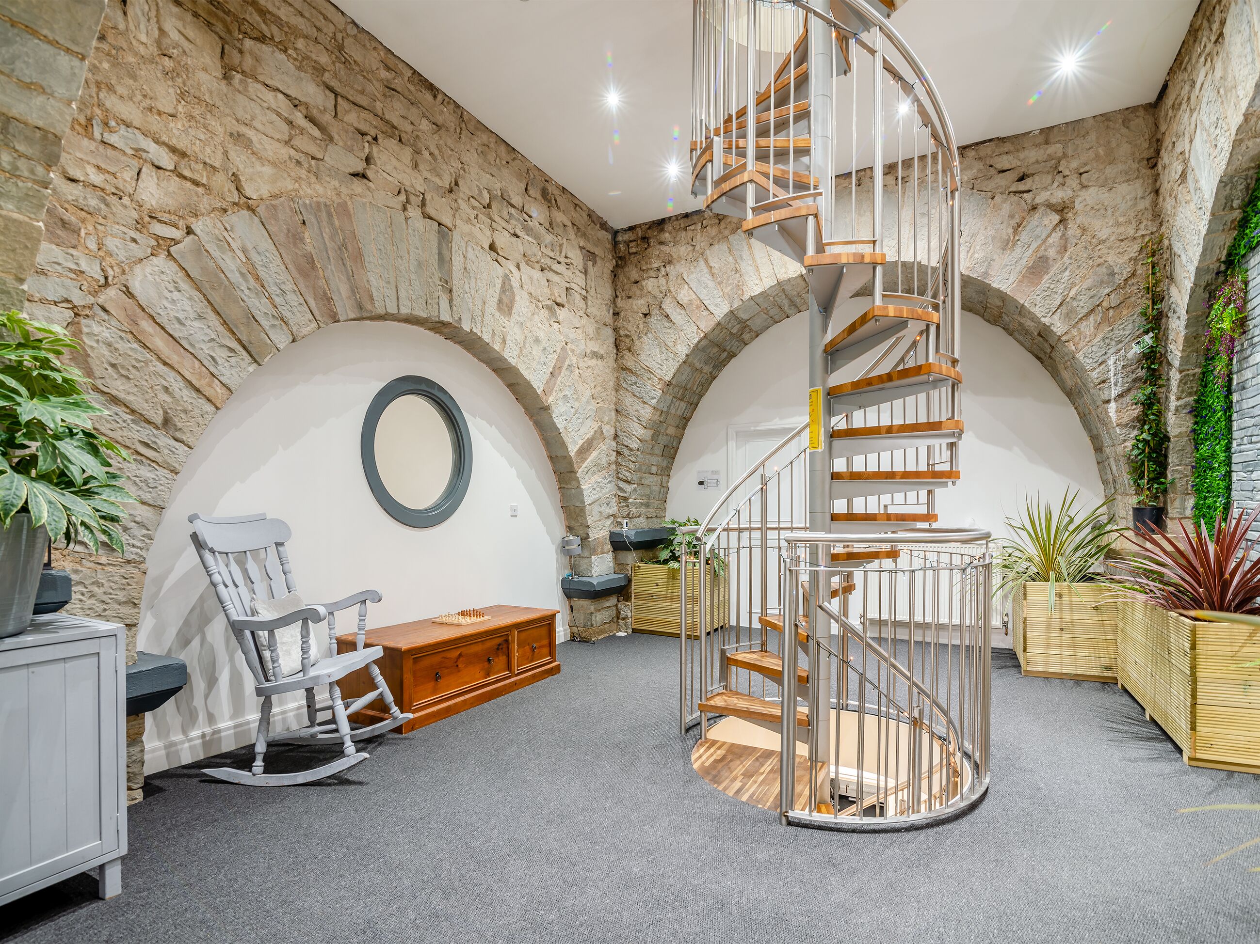 A modern interior with a spiral staircase, stone walls, and a cozy seating area with a rocking chair and chessboard.