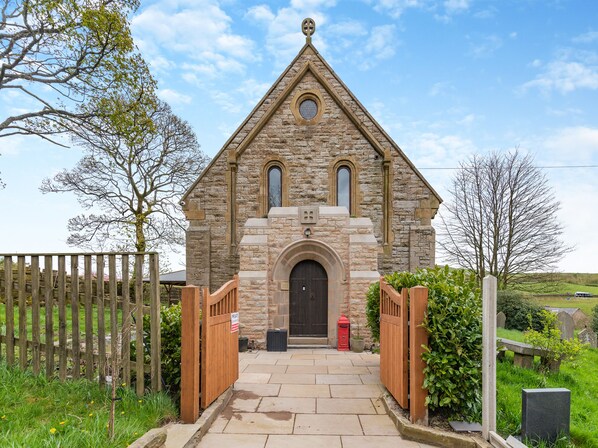 A stone church with a pointed roof, a central arched entrance, and a small circular window above the door.