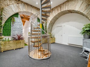 A spiral staircase with a stone wall backdrop, a white door, and a radiator.