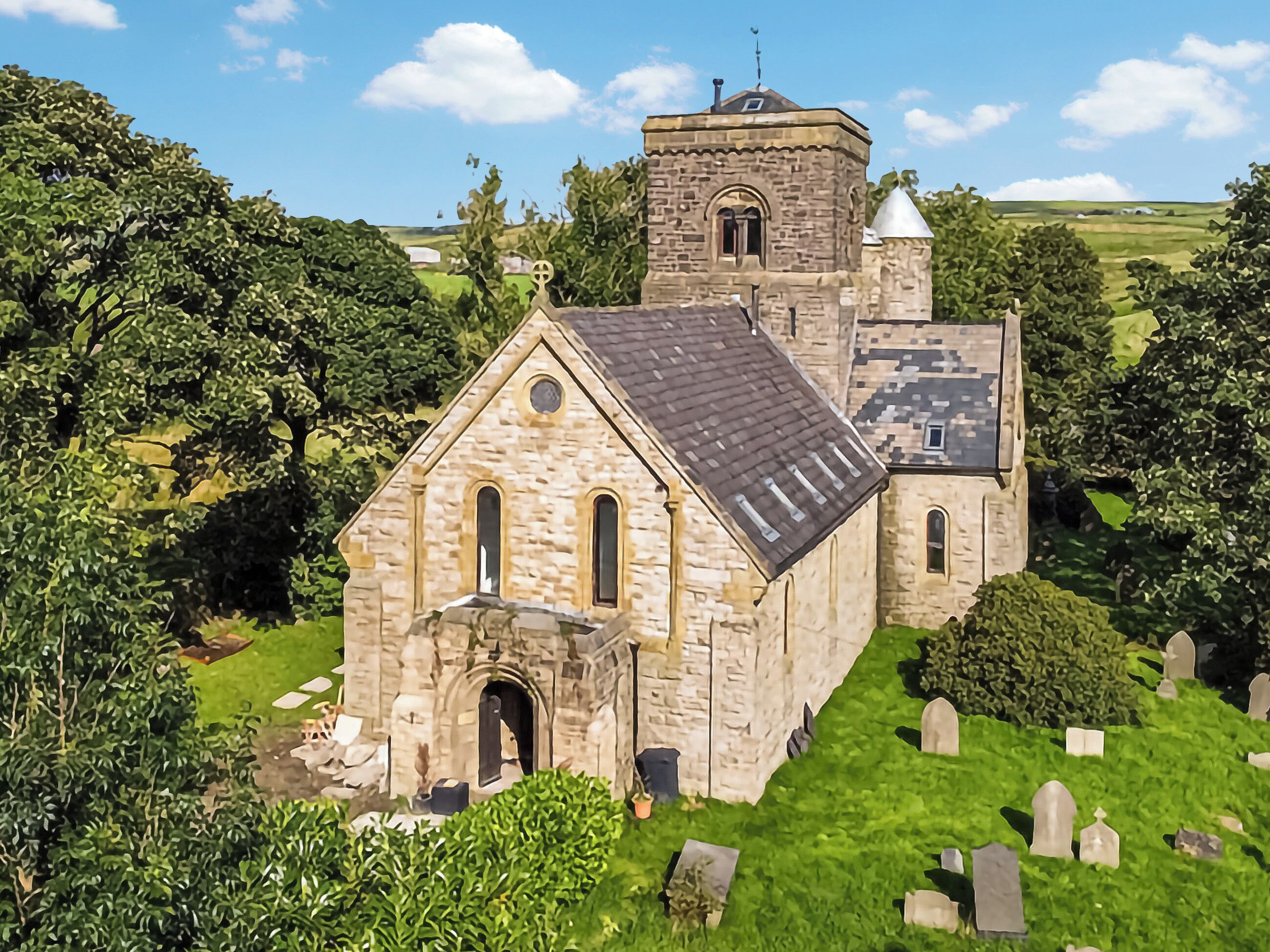 A stone church with a bell tower, surrounded by greenery and a cemetery.