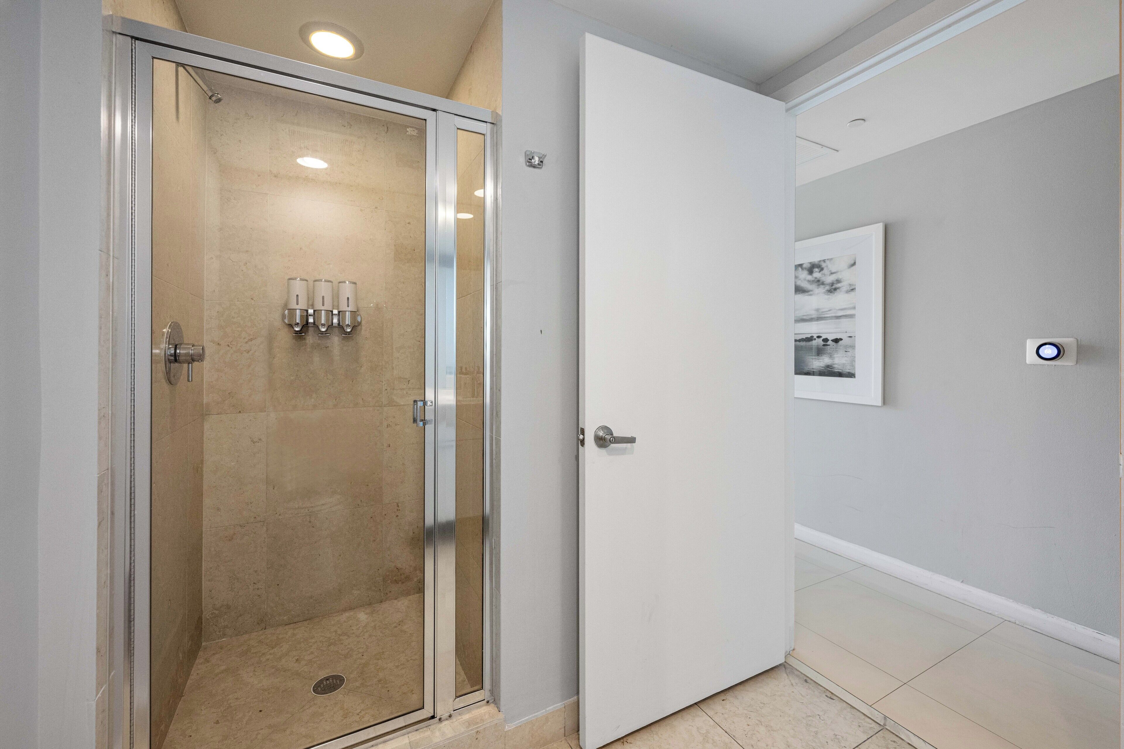 A modern bathroom with a glass shower enclosure, a white door, and a framed picture on the wall.