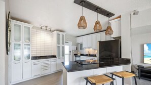 Una cocina moderna con armarios blancos, encimera negra y tres lámparas colgantes de mimbre.