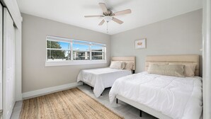 Un dormitorio con dos camas, un ventilador de techo, una ventana con persianas y una alfombra tejida.