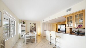 A modern kitchen with white cabinetry, a dining area with a white table and chairs, and a small bar area with stools. - Ocean Front Beach in Clearwater 2BB 2BA  (Clearwater Beach)