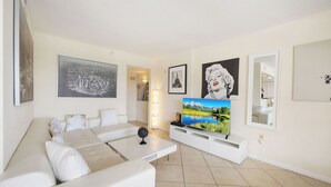 A modern living room with a white sofa, a flat-screen TV, and artwork on the walls. - Ocean Front Beach in Clearwater 2BB 2BA  (Clearwater Beach)