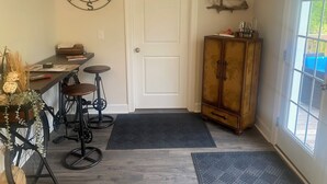 Een kamer met een witte deur, een kompas als wanddecoratie, een houten kast en een klein tafeltje met krukken.