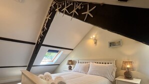 Une chambre avec un plafond en pente, un lit recouvert de draps blancs, deux lampes de chevet et une petite fenêtre.