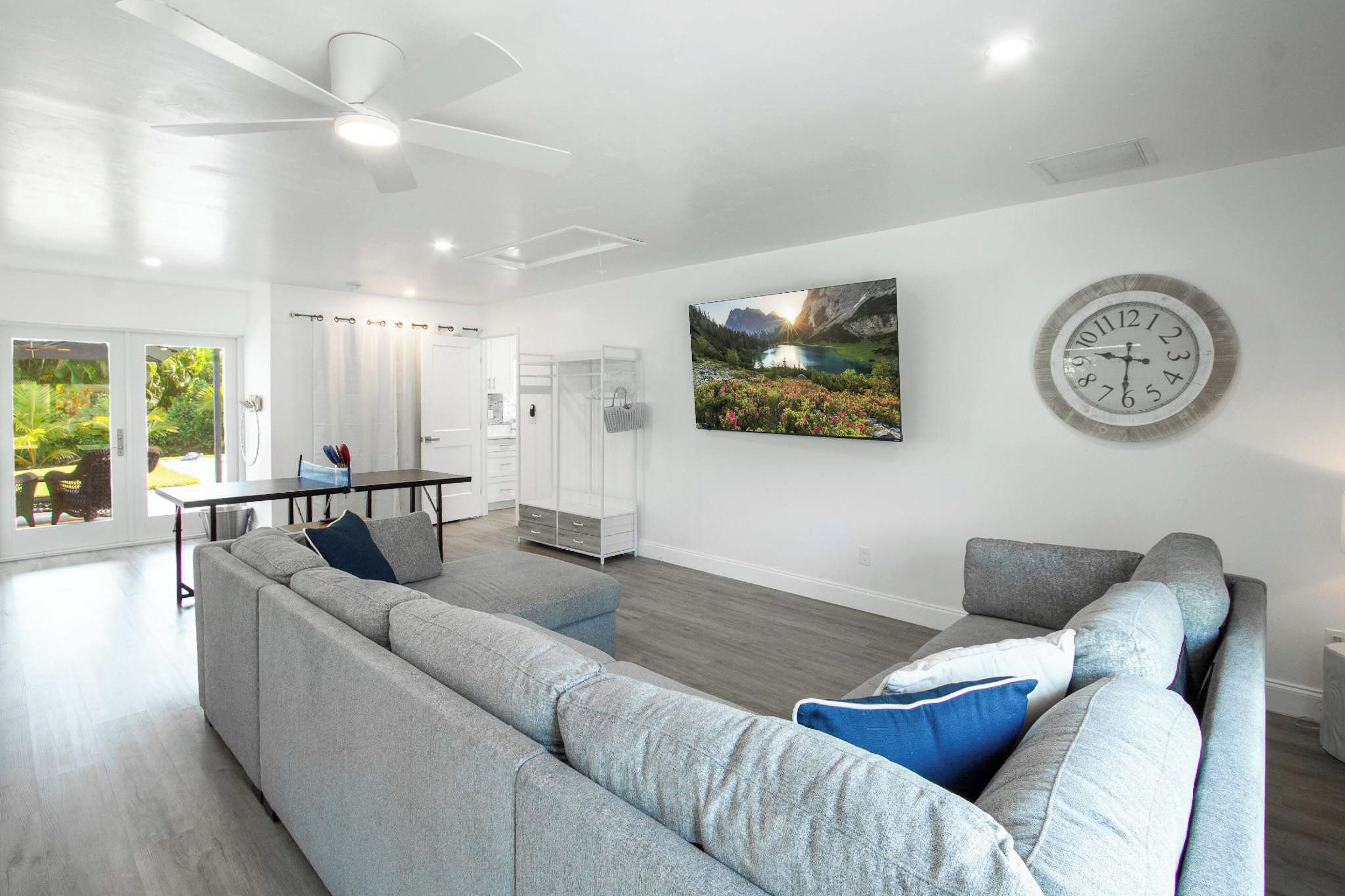 Een moderne woonkamer met een grijze modulaire bank, een eettafel en een grote wandklok.