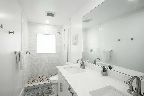 A modern bathroom with a large mirror, two sinks, and a shower.