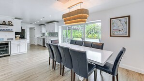 A modern kitchen with white cabinetry, a large island, and a dining area with a white table and dark chairs. - Naples Escape w/ Furnished Patio & Private Pool! (Naples)