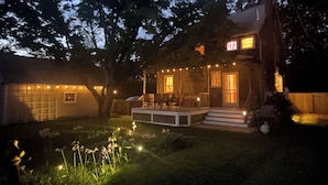 Una casa de dos pisos con un porche, luces colgantes y un pequeño jardín.