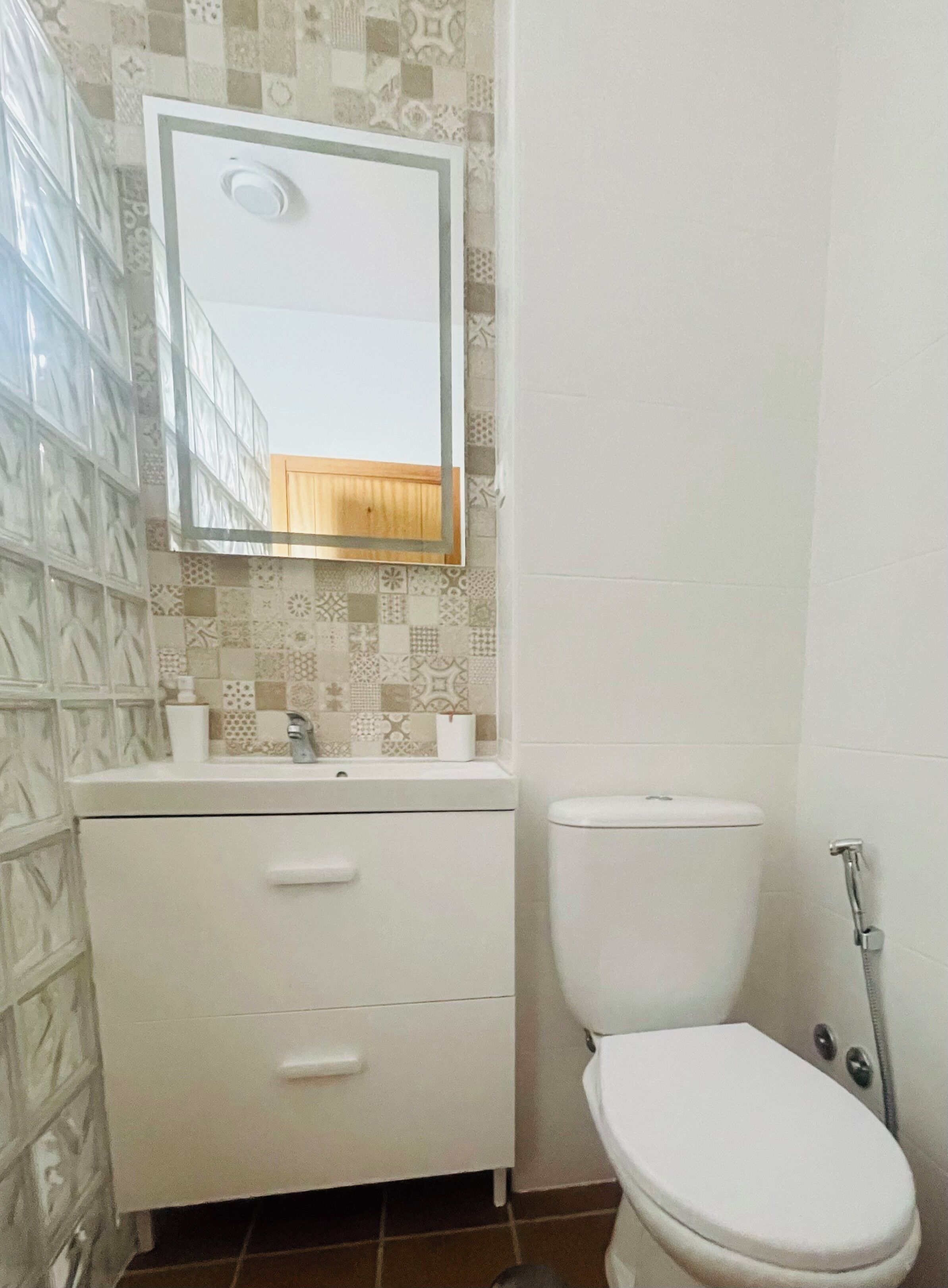 A bathroom with a tiled wall, a white sink with a mirror, a toilet, and a shower area.