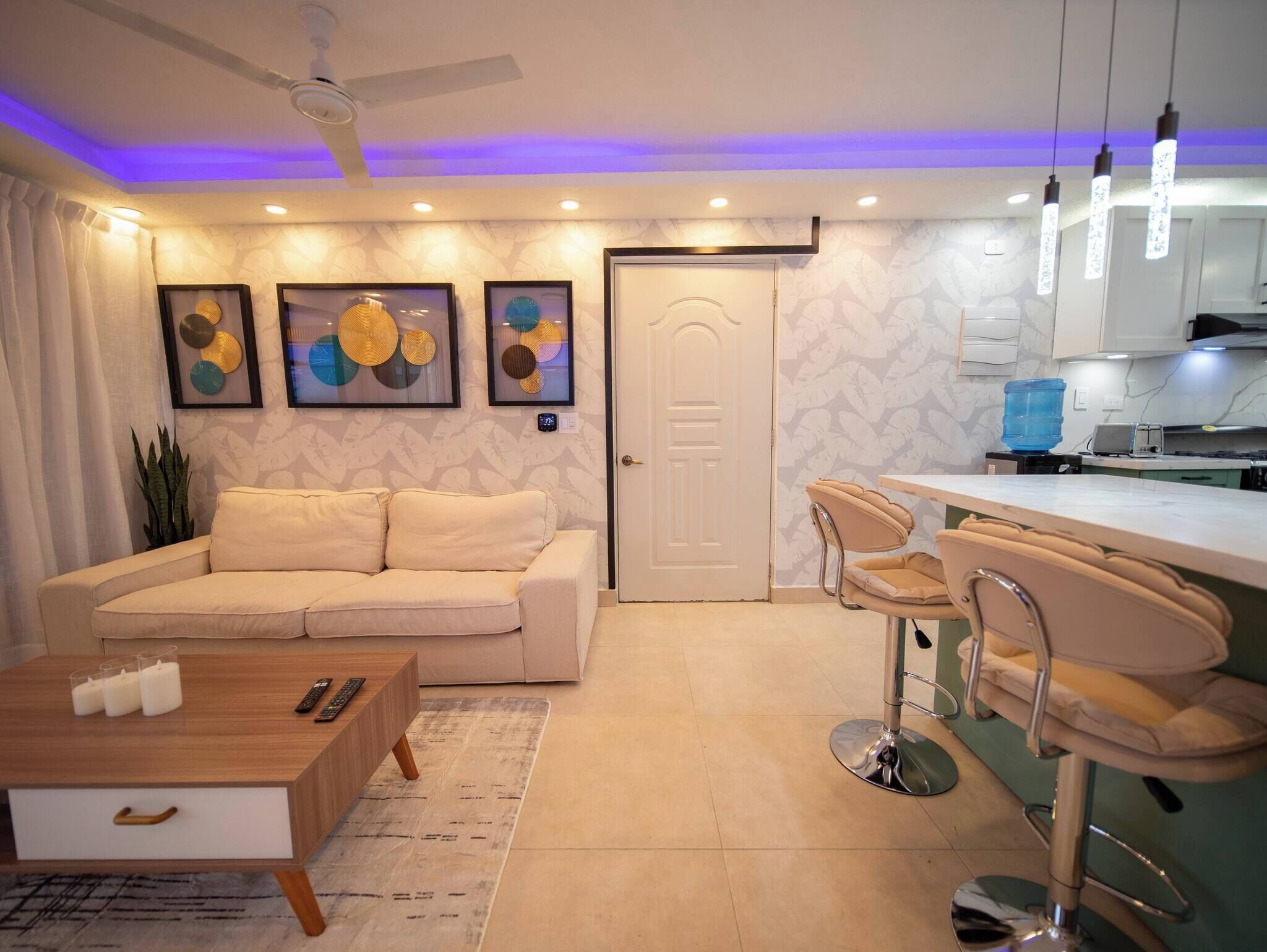 A modern living room with a sofa, coffee table, and a dining area with bar stools.