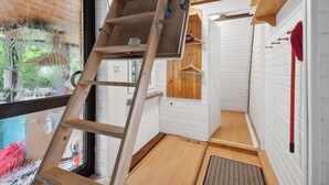 A room with a wooden ladder, a wooden door, a wooden shelf, and a red hanger on the wall.