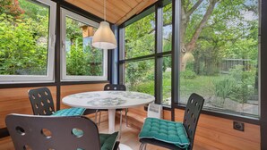 A conservatory with a round table and chairs, large windows, and a hanging light fixture.