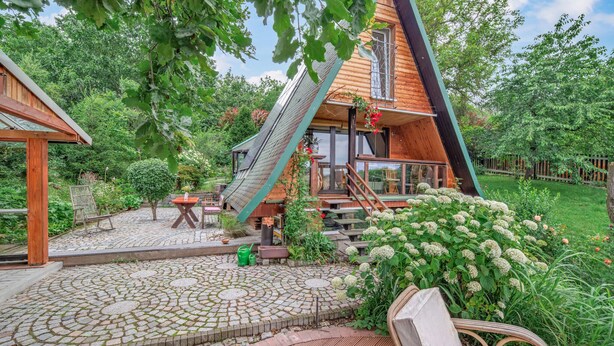 A wooden house with a steeply pitched roof, a wooden deck, and a stone patio area.