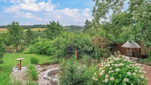 A garden with a stone pathway, a wooden pergola, and a view of the countryside.