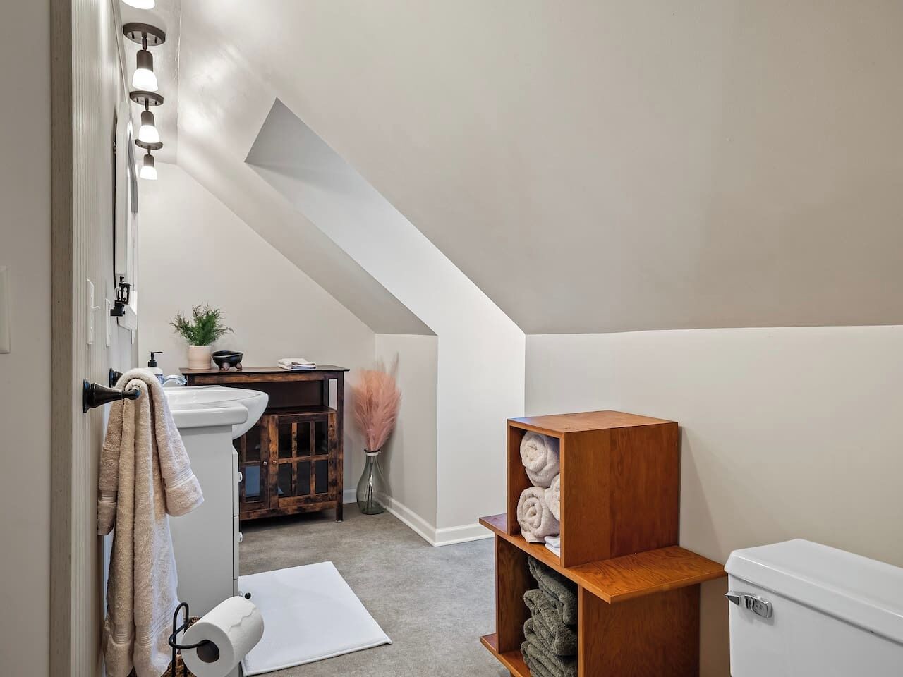 A bathroom with a white sink, a towel rack, a wooden shelf with towels, a toilet, and a shower area.