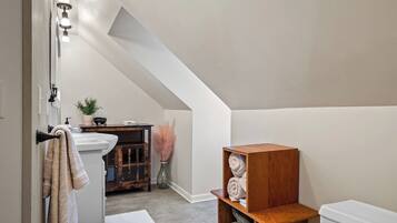 A bathroom with a white sink, a towel rack, a wooden shelf with towels, a toilet, and a shower area.