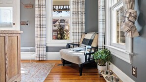 Un salon chaleureux avec un meuble en bois, un fauteuil à motifs écossais, une petite table avec une plante et une fenêtre avec des rideaux.