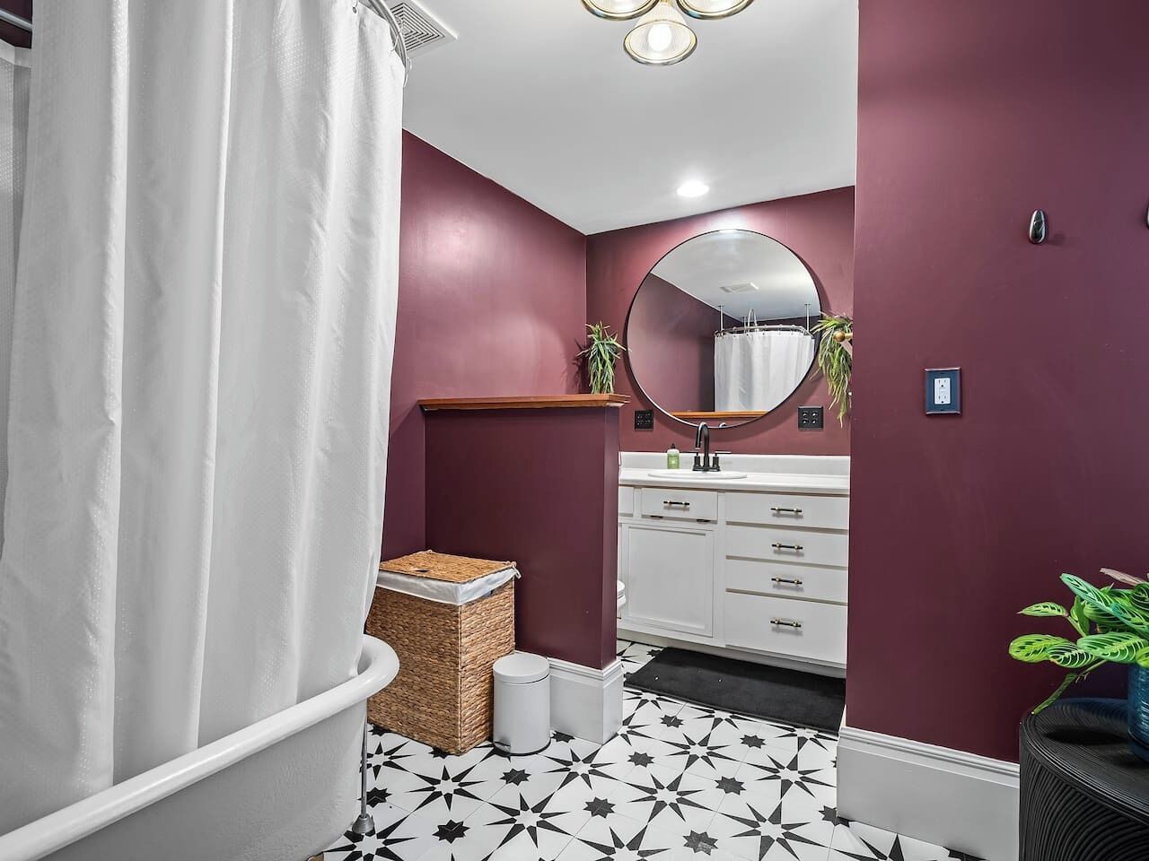 Un bagno con una vasca da bagno bianca, uno specchio rotondo sopra il lavabo e un mobile vanitario bianco con cassetti.