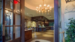 Um saguão de hotel com uma mesa de recepção de madeira, área de bar e um candelabro.