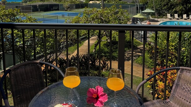 Un balcón con una mesa dispuesta para dos, con vistas a una piscina y palmeras.