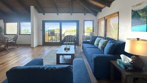 Un espacio habitable amplio con un sofá, una mesa de centro y una lámpara. Amplias ventanas ofrecen vistas al exterior.