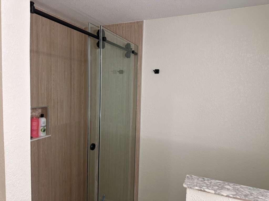 Een badkamer met een douchecabine van glas, een houten wastafelmeubel en een plank met toiletartikelen.
