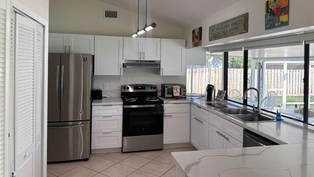 A kitchen with white cabinets, stainless steel appliances, a window with a view, and a ceiling light fixture. - Port St Lucie 3BD -2B (Port Saint Lucie)