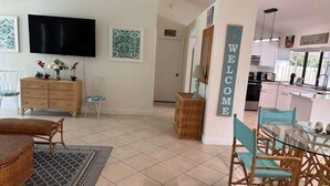 A modern living room with a TV, a dining area with a glass table, and a kitchen visible through an open door. - Port St Lucie 3BD -2B (Port Saint Lucie)