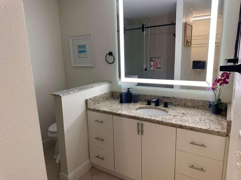 A bathroom with a large mirror, a sink, and a toilet.