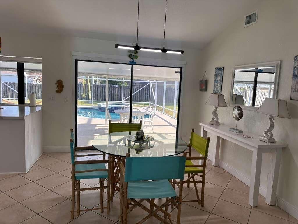 Un coin repas avec une table et des chaises en verre, une console blanche agrémentée de lampes, et une vue sur une piscine à travers de grandes portes vitrées.
