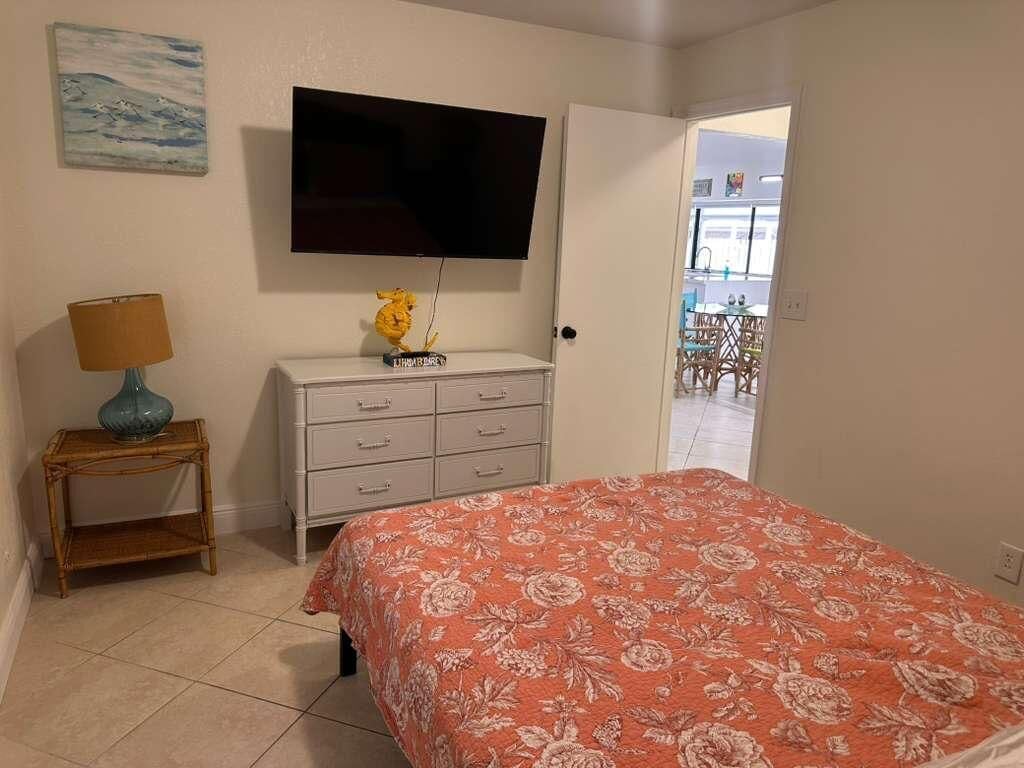 Un dormitorio con una cama, televisión, cómoda y una puerta que da a un balcón.