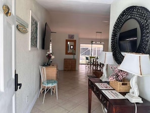 A room with a dining area, a TV mounted on the wall, a large mirror, and a table with a lamp and decorative items. - Port St Lucie 3BD -2B (Port Saint Lucie)