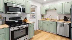Cucina con pensili verde chiaro, elettrodomestici in acciaio inossidabile, lavello e lavastoviglie.