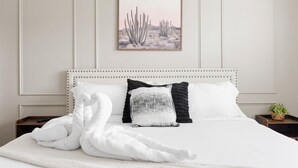 Un letto rifatto con lenzuola bianche, una testiera con motivo decorativo e un quadro con saguaro appeso al muro.