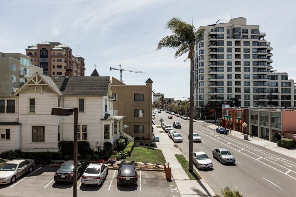 Une vue de rue avec des immeubles d’habitation, des voitures garées et un grand bâtiment moderne.