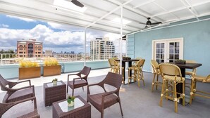 Terraço no telhado com móveis de vime, uma mesa de jantar e plantas em vasos.