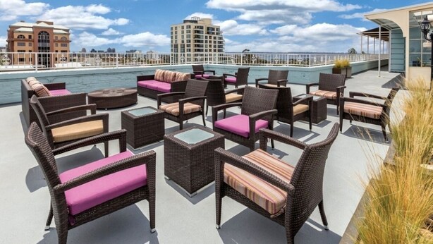 Eine Dachterrasse mit Korbmöbeln, Blick auf das Wasser und Gebäude im Hintergrund.