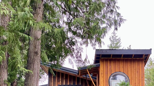 Una cabaña de madera con un ventanal grande, un tragaluz circular y una terraza de madera.