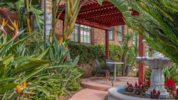 A garden with a fountain, a brick building, and a covered patio area. - San Diego | Parkside Weekend | Hot Tub & Rooftop Deck (San Diego)