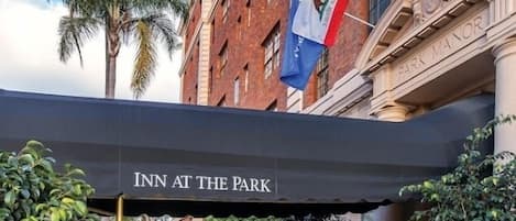 A hotel entrance with a covered walkway, palm trees, and flags.