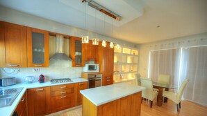 Una cocina moderna con armarios de madera, una isla central y una zona de comedor con mesa y sillas de vidrio.