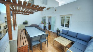 Una terraza en la azotea con una pérgola de madera, una mesa de comedor con sillas, un sofá y plantas en macetas.