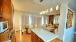 Una cocina moderna con armarios de madera, encimera blanca y una zona de comedor con mesa y sillas de vidrio.