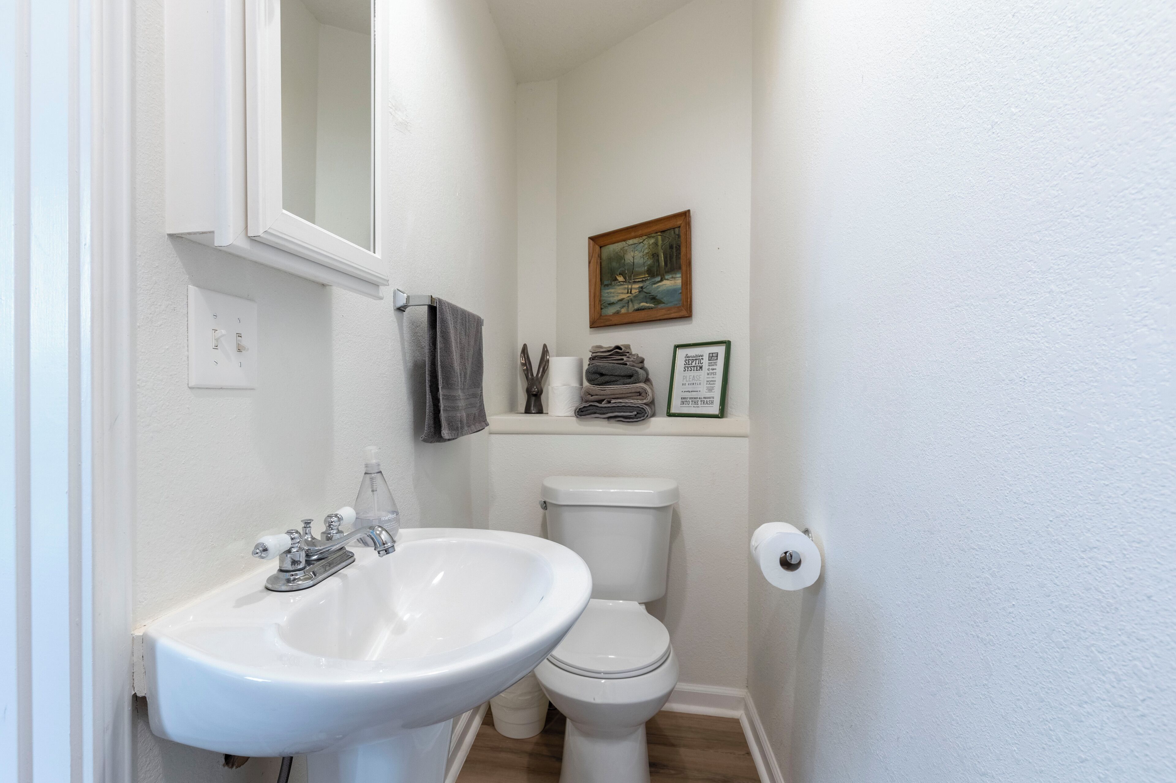 Ein kleines, sauberes Badezimmer mit einem weißen Waschbecken, einer Toilette und einem gerahmten Bild an der Wand.