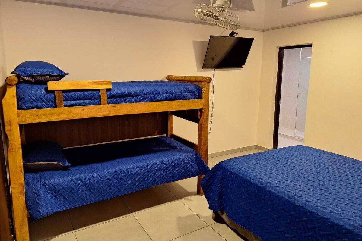 A bunk bed with blue bedding, a television mounted on the wall, and a window with blinds.